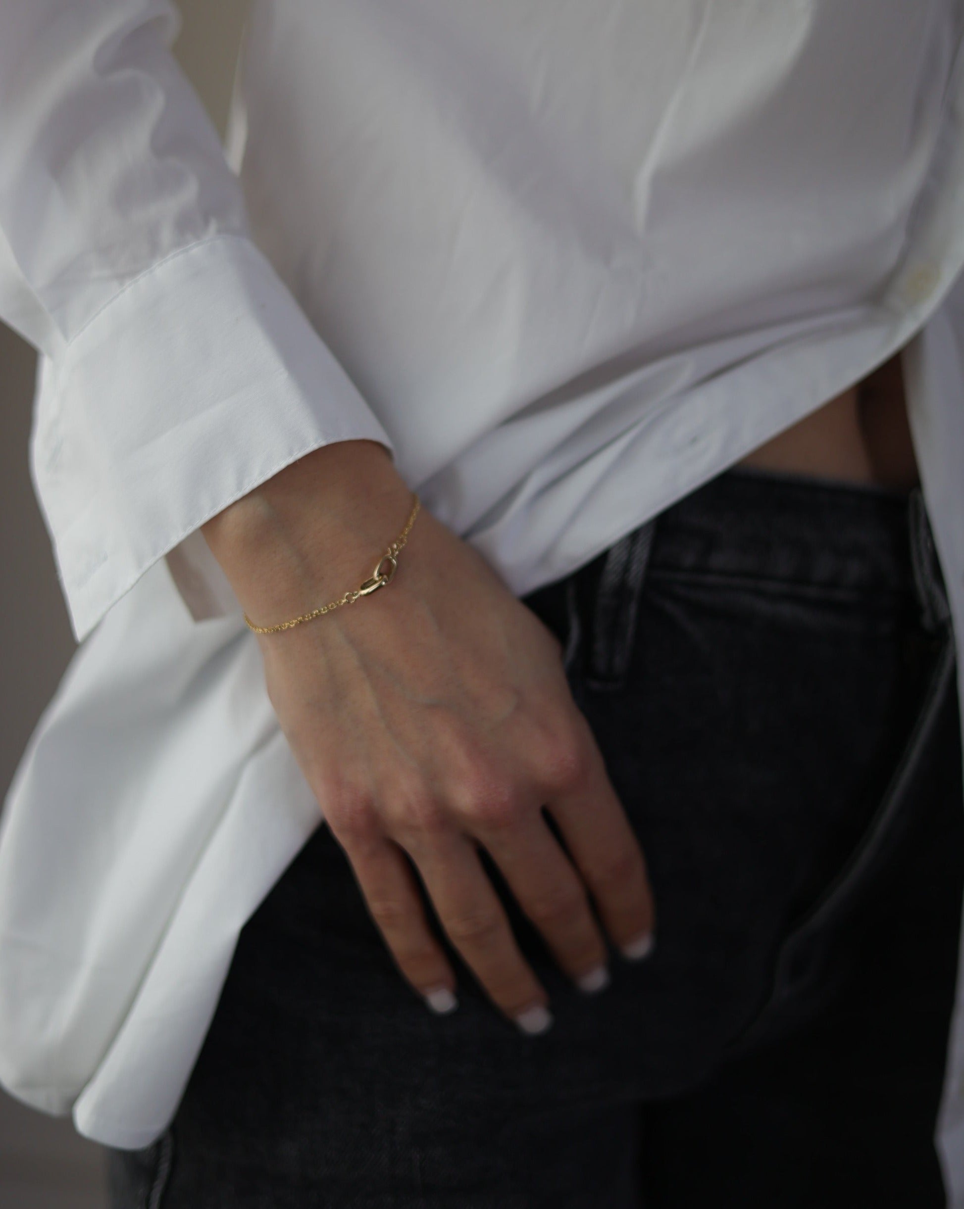 women in a white dress shirt and black jeans wearing a 14 karat gold bracelet with a interlocking clasp