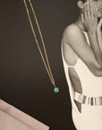 14k gold chain and green stone charm on a black magazine background