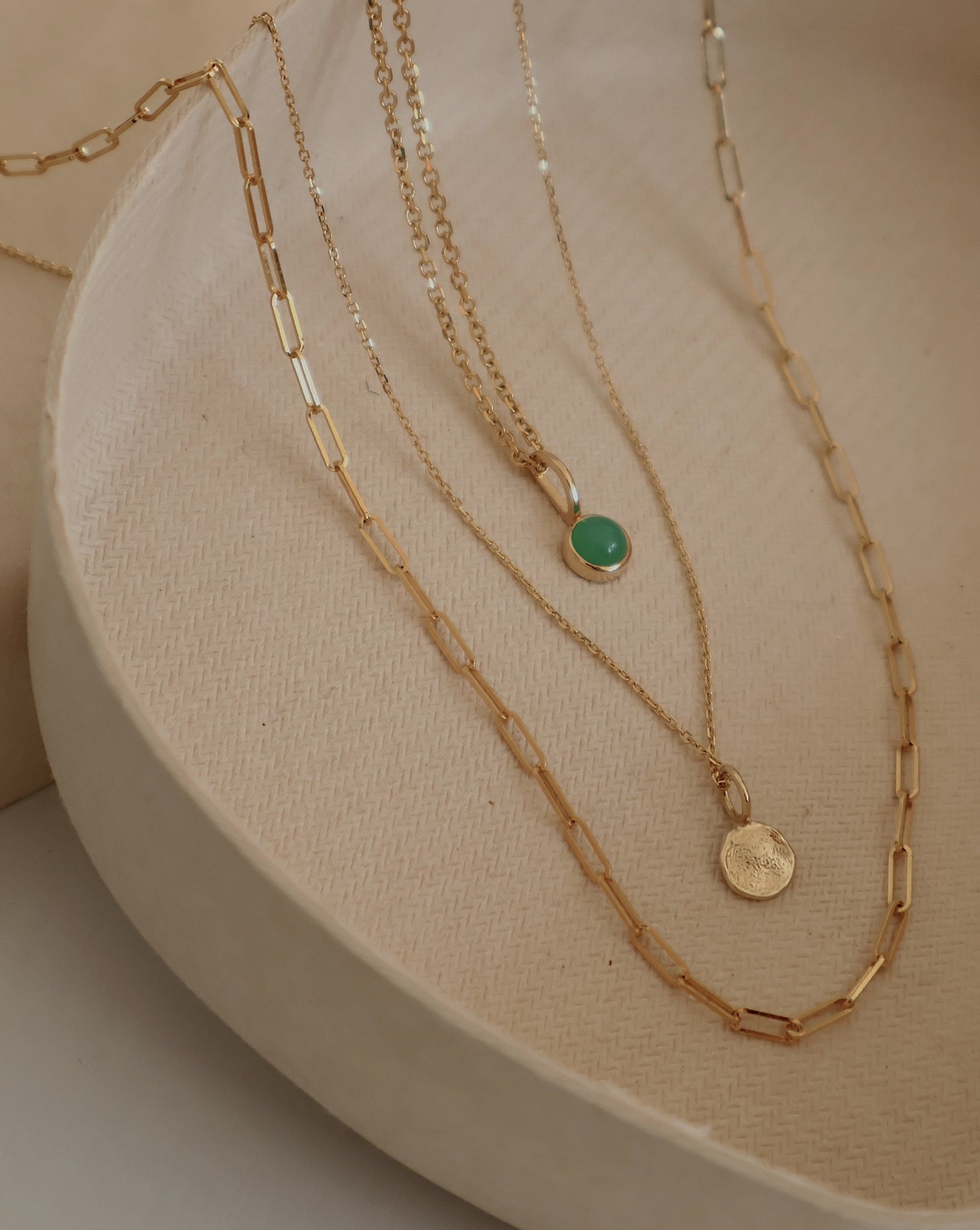 Three 14k gold chains on a clay dish: paperclip chain, dainty cable chain, and bevel cut cable chain.