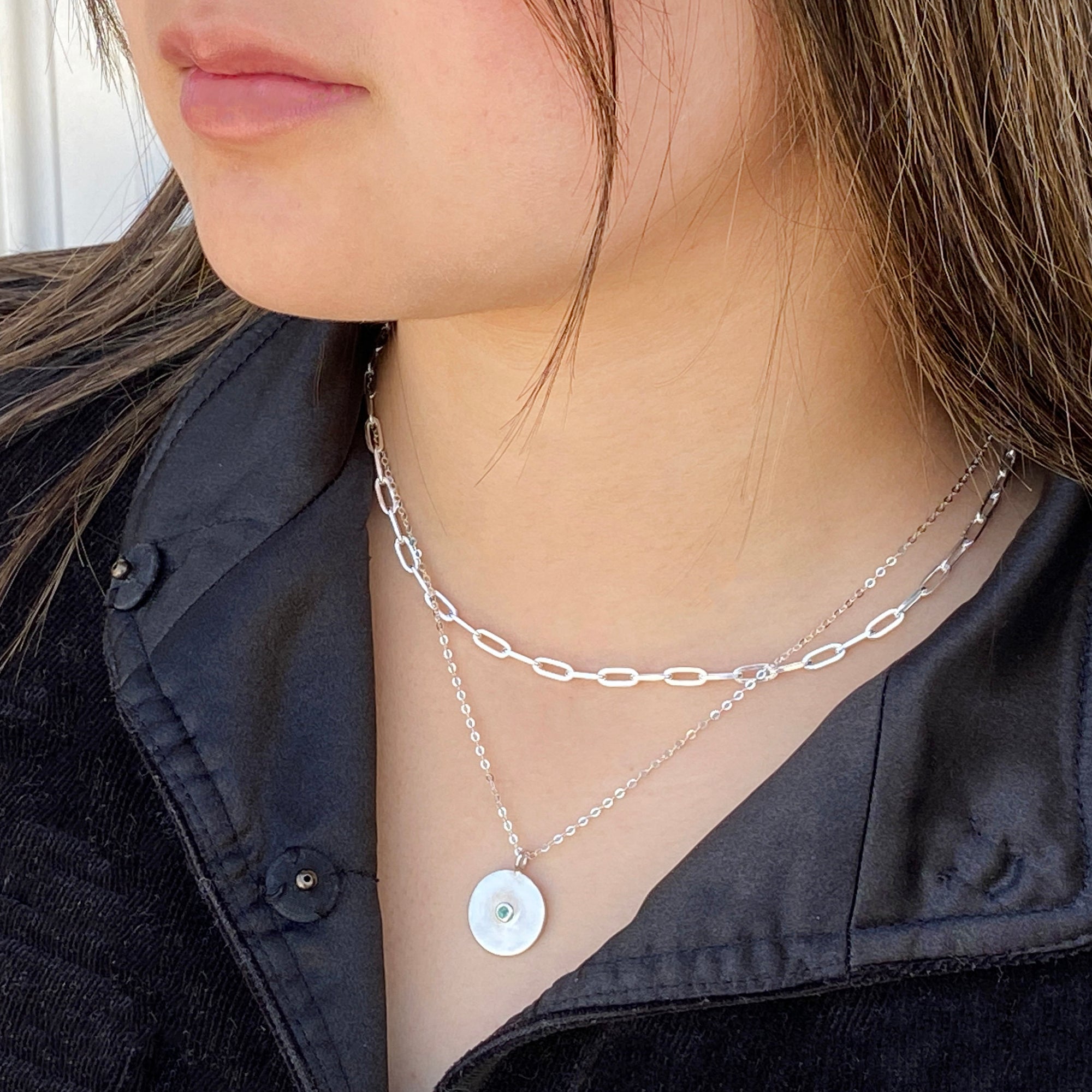 women wearing two silver necklaces with an emerald pendant