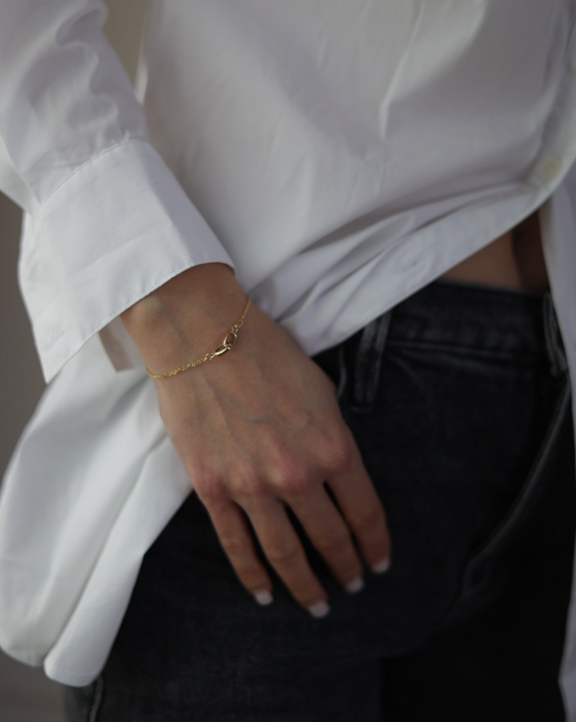 women in a white dress shirt and black jeans wearing a 14 karat gold bracelet with a interlocking clasp 