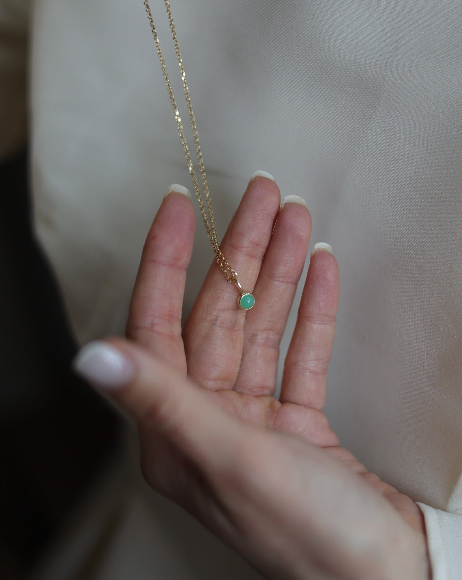 women&#39;s hand showing off a crystal charm pendant on a 14k gold chain necklace