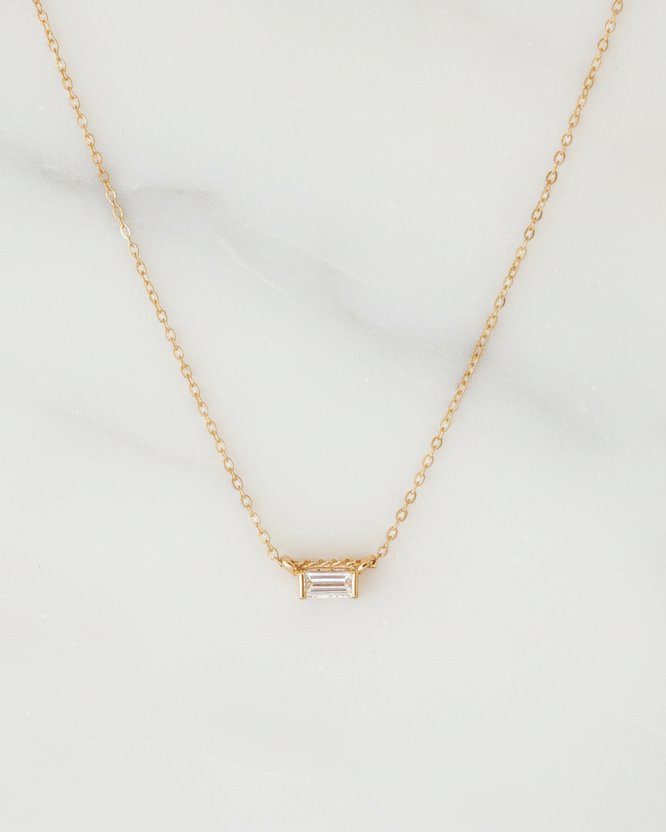 14k Gold dainty chain necklace with a lab grown diamond baguette charm on a marble background, fine jewelry by Sincerely Chain Co.
