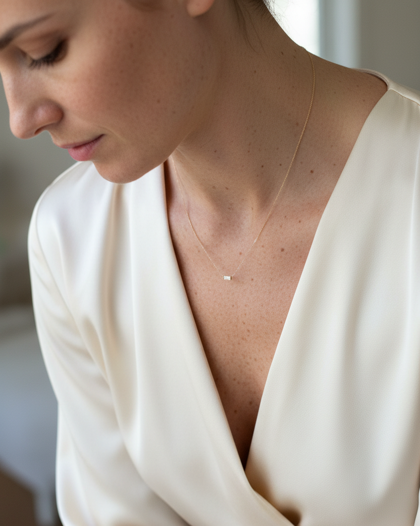 Women wearing a 14k gold thread necklace with a tiny baguette diamond pendant, styled with a silk ivory wrap blouse.