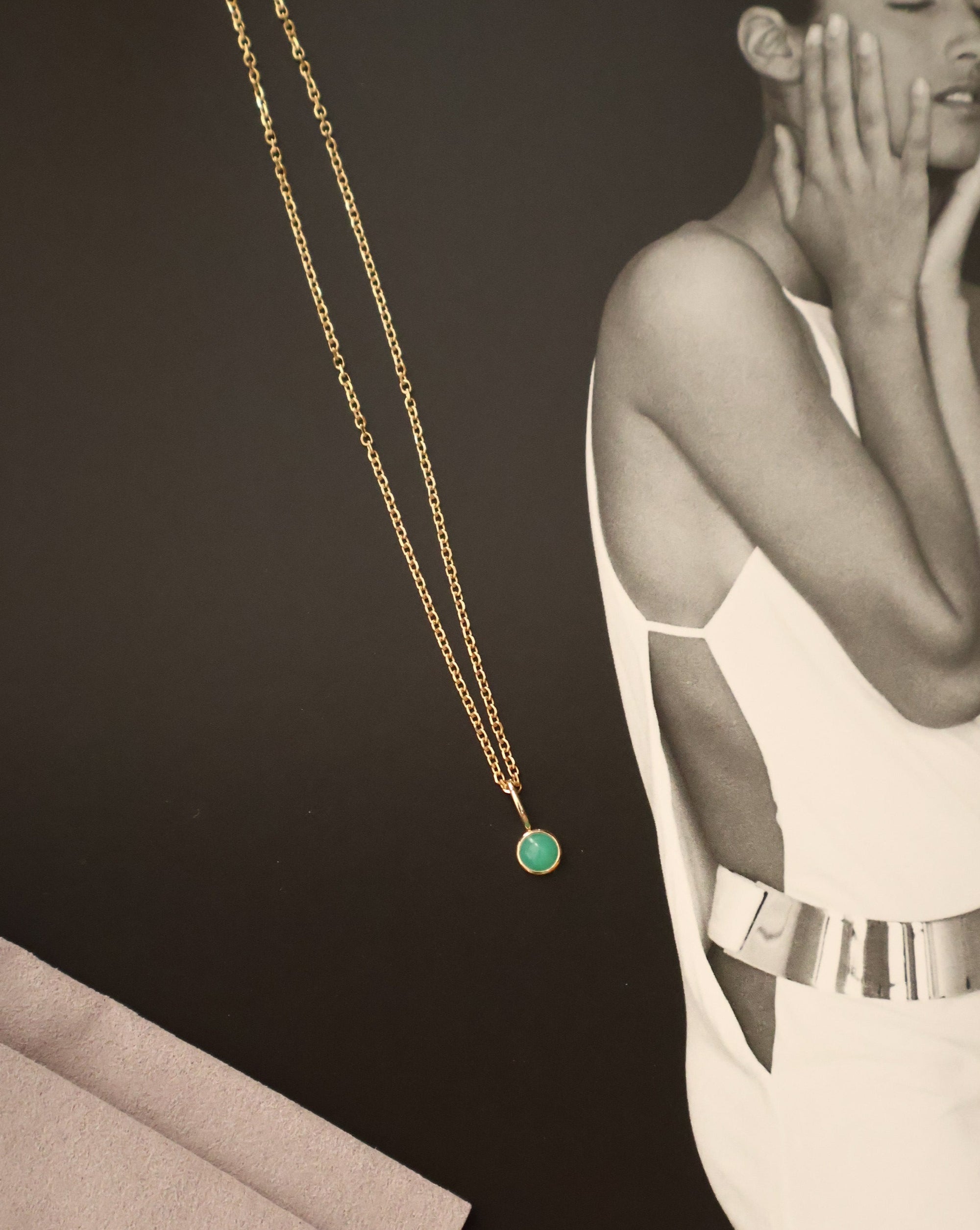 14k gold chain and green stone charm on a black magazine background, modern jewelry by Sincerely Chain Co.