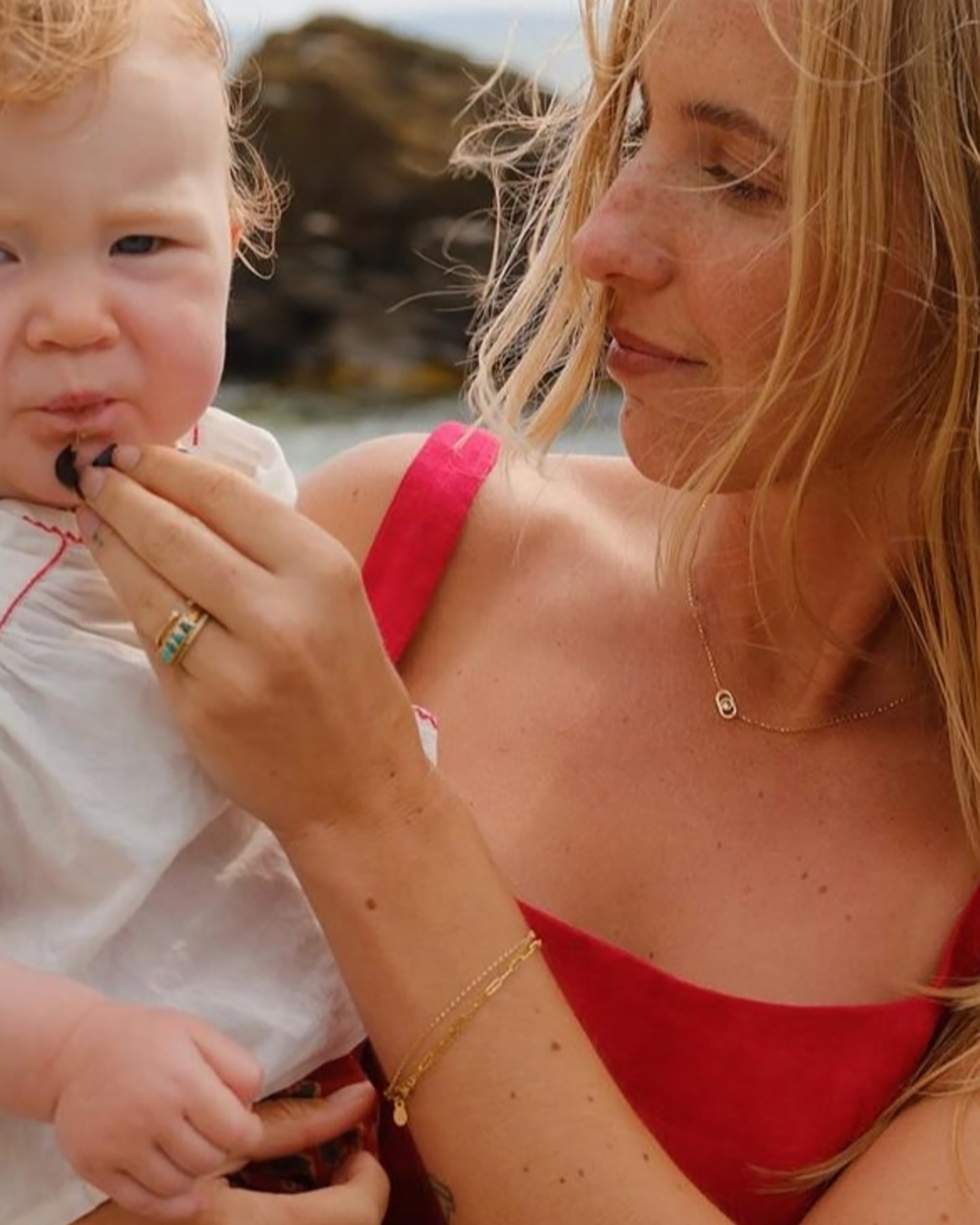 Mother wearing solid 14k gold dainty necklace and layered gold bracelets by Sincerely Chain Co. while holding her baby outdoors.