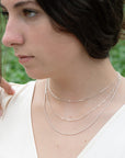 A young women wearing a dainty silver layering necklace with three chains, including a snake chain, a paperclip, and a dainty cable chain necklace, minimalist jewelry by Sincerely Chain Co.