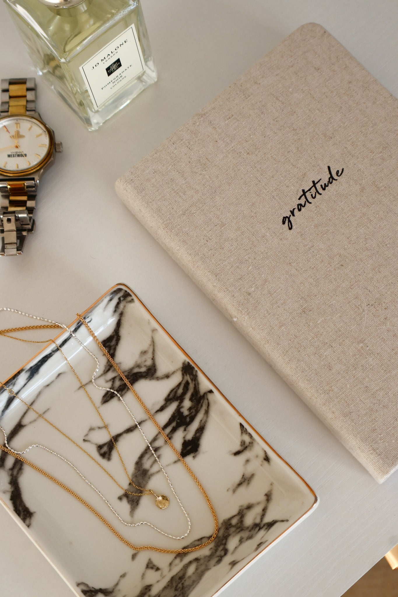 Table arrangement with perfume, watch, gratitude journal and gold necklaces by Sincerely Chain Co.