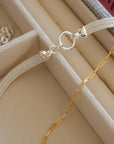 A soft cloth jewelry box with a sterling silver mesh necklace and gold paperclip.