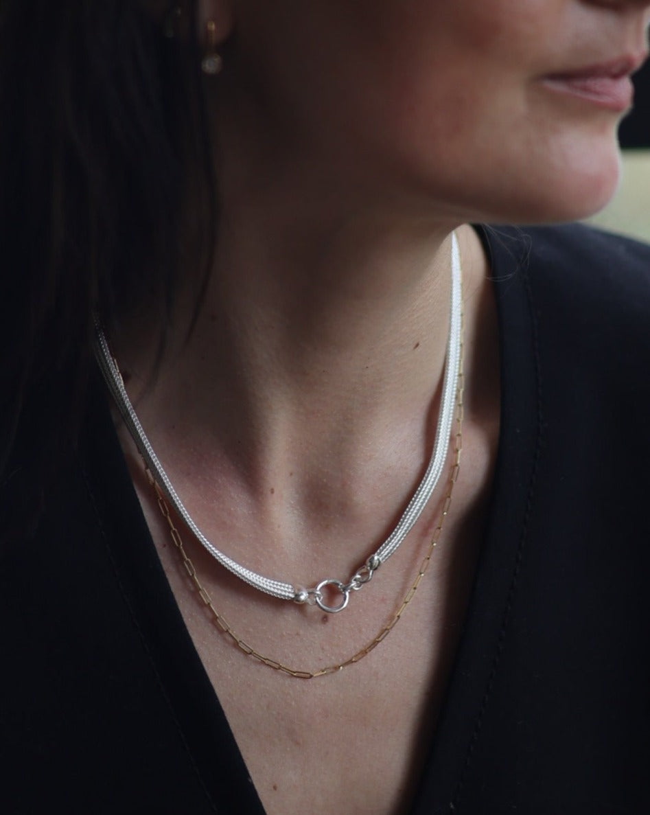 A women wearing a sterling silver foxtail mesh necklace with circle feature clasp, paired with a dainty gold paperclip chain necklace.