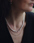 A women wearing a sterling silver foxtail mesh necklace with circle feature clasp, paired with a dainty gold paperclip chain necklace.
