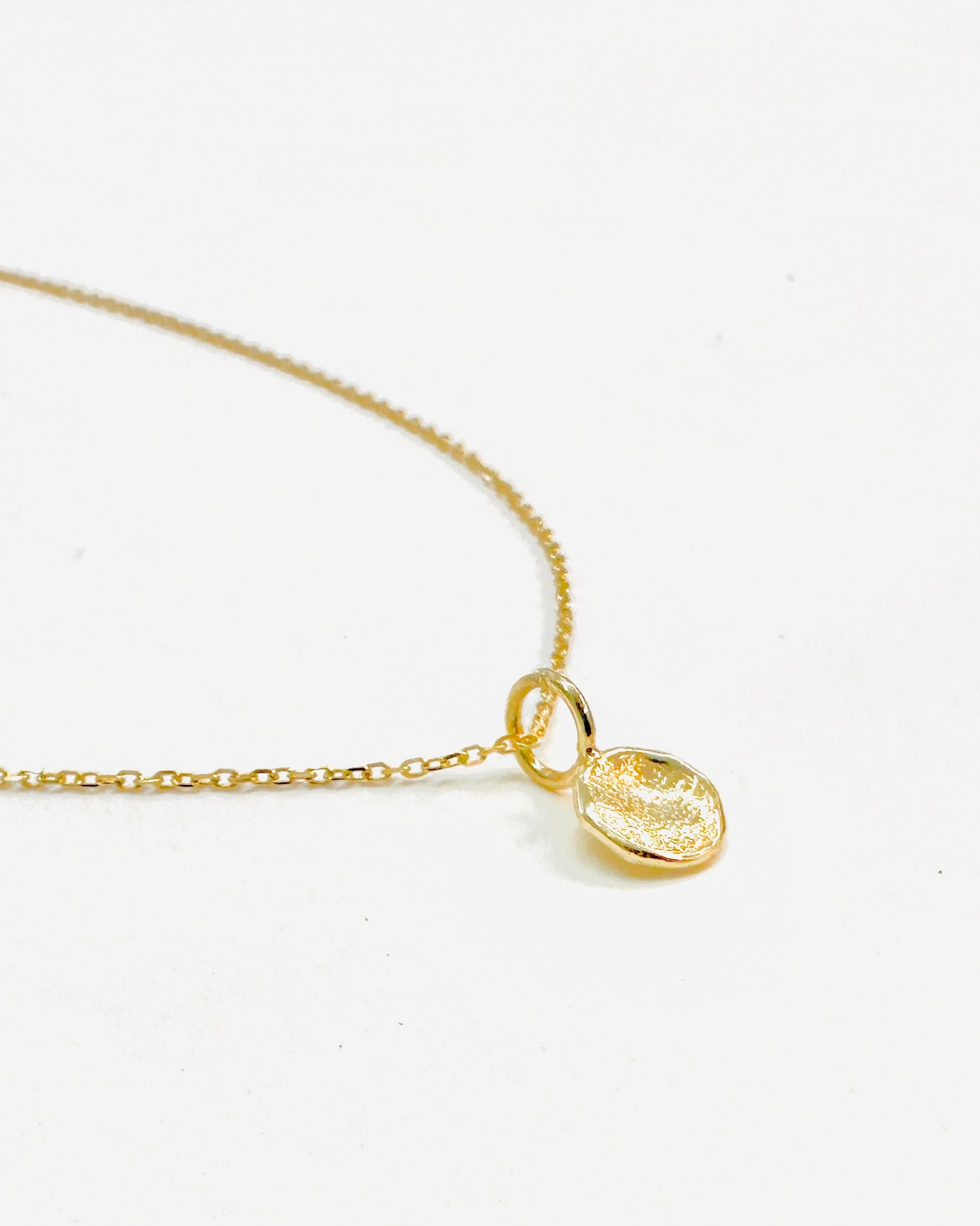 solid gold mini disc pendant with subtle texture on a delicate 14k gold chain