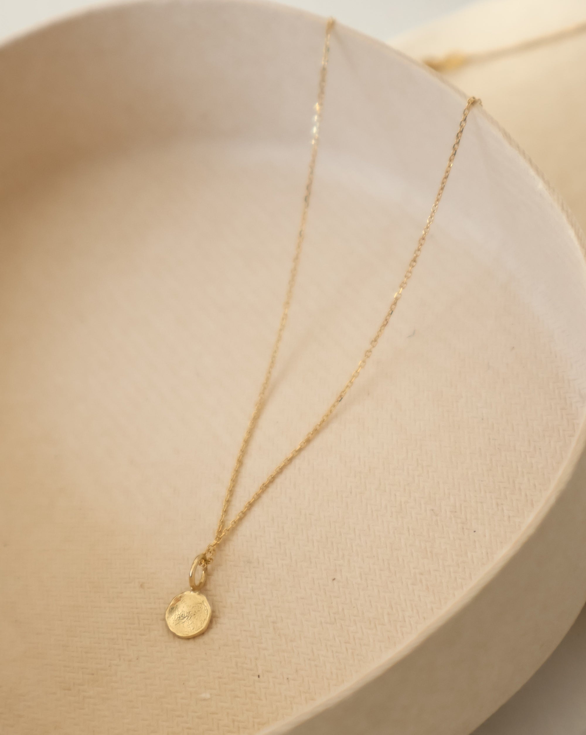 solid gold mini disc pendant  on a delicate 14k gold chain in a clay dish