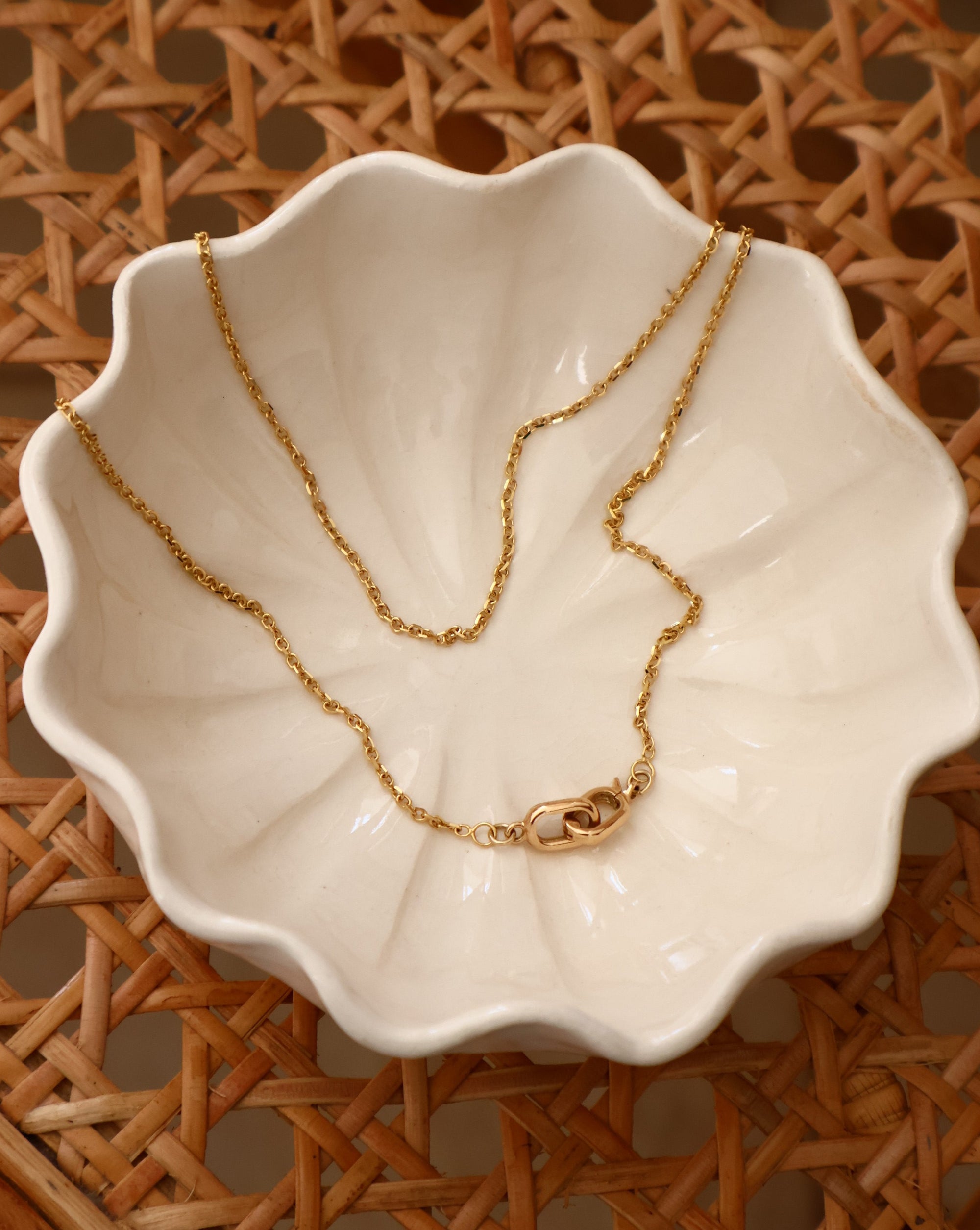 14k gold necklace in a white shell dish on a wicker chair