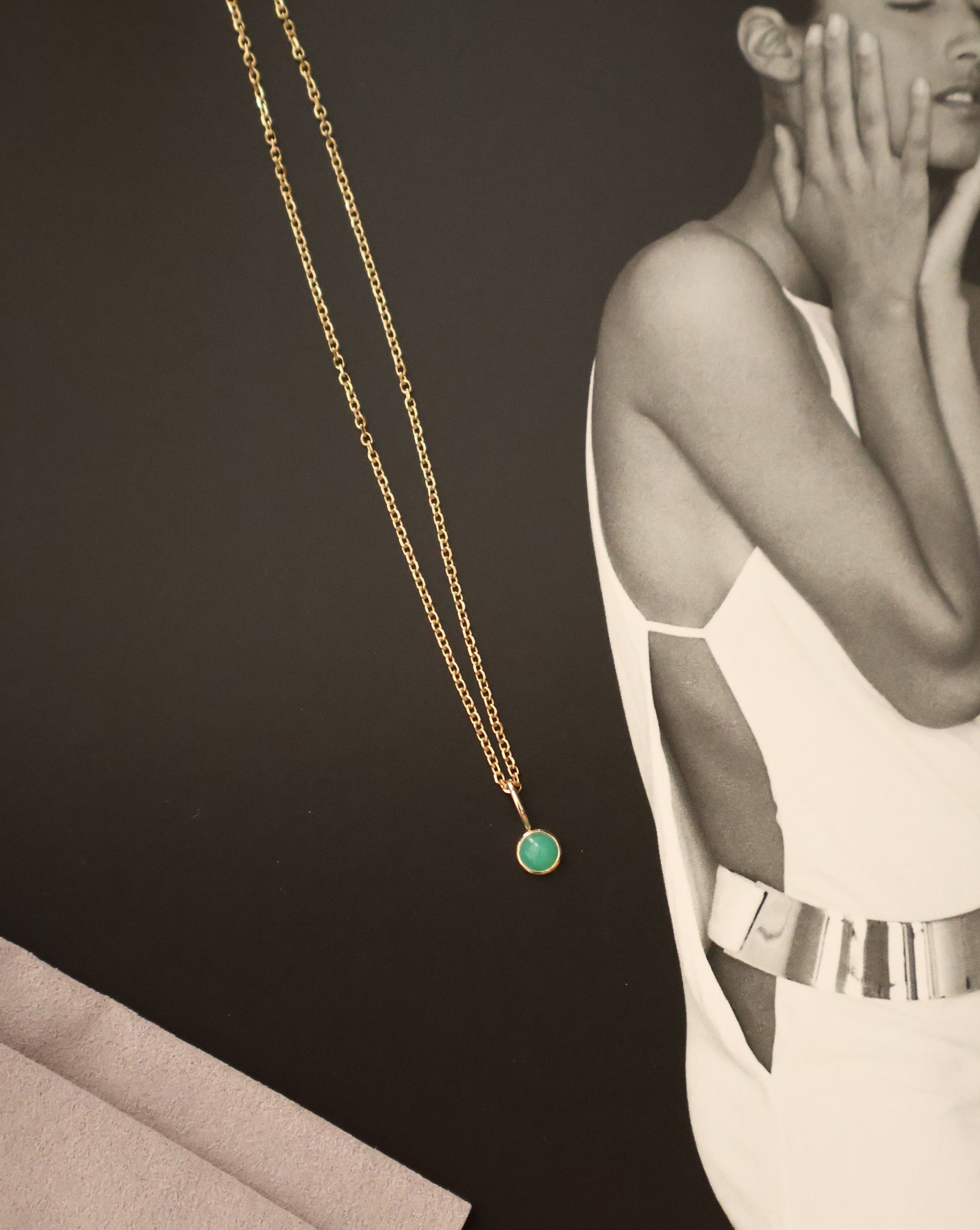 14k gold chain and green stone charm on a black magazine background