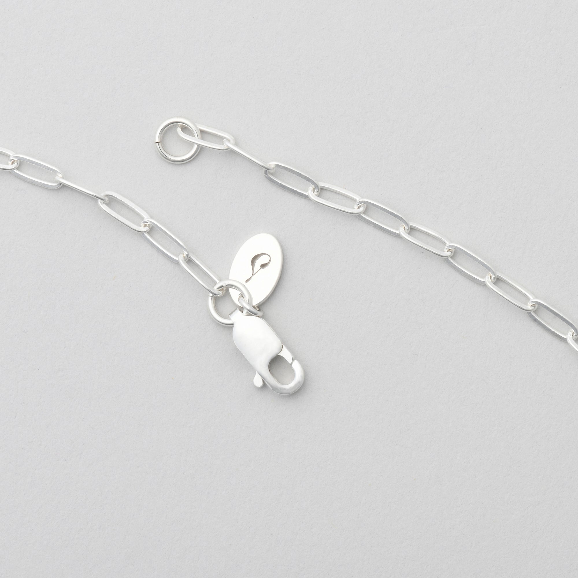 A sterling silver necklace with a delicate paperclip chain design and a branded lobster clasp closure, minimalist jewelry by Sincerely Chain Co.