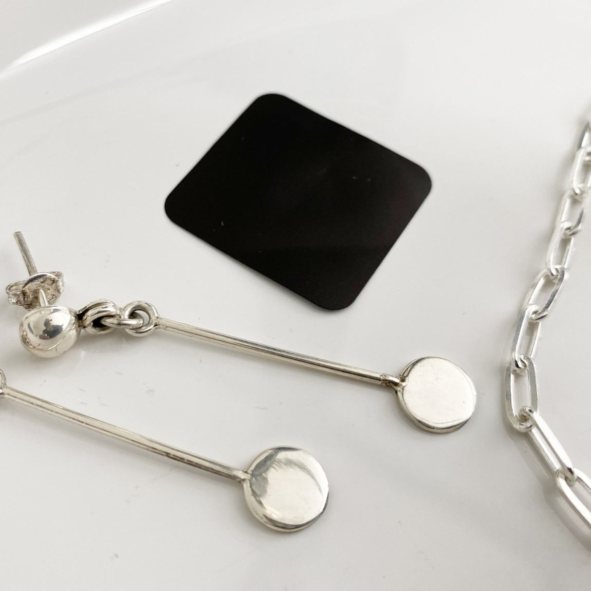 small black anti-tarnish tabs next to silver jewelry on a white dish