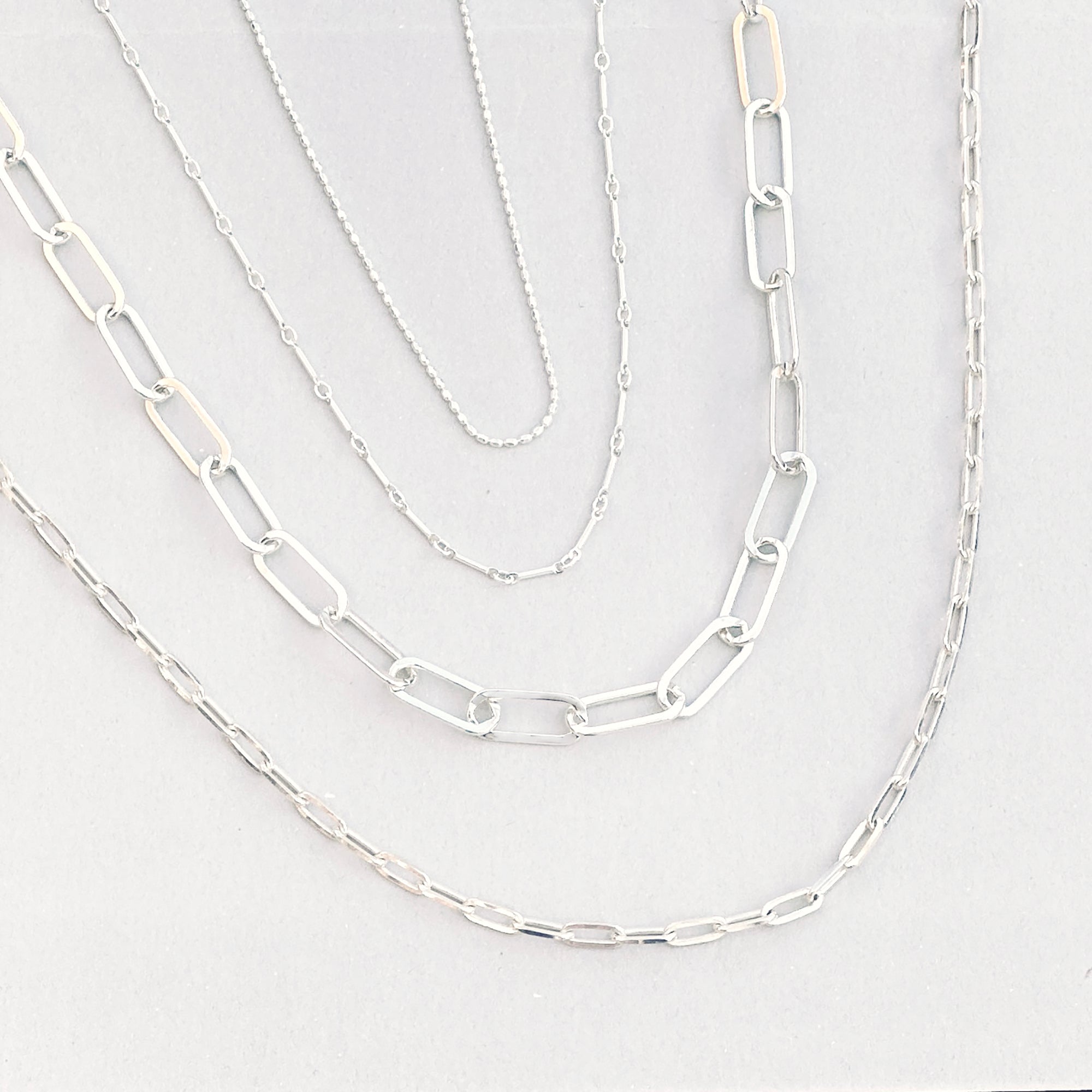 four silver necklaces layered to make a premade necklace stack