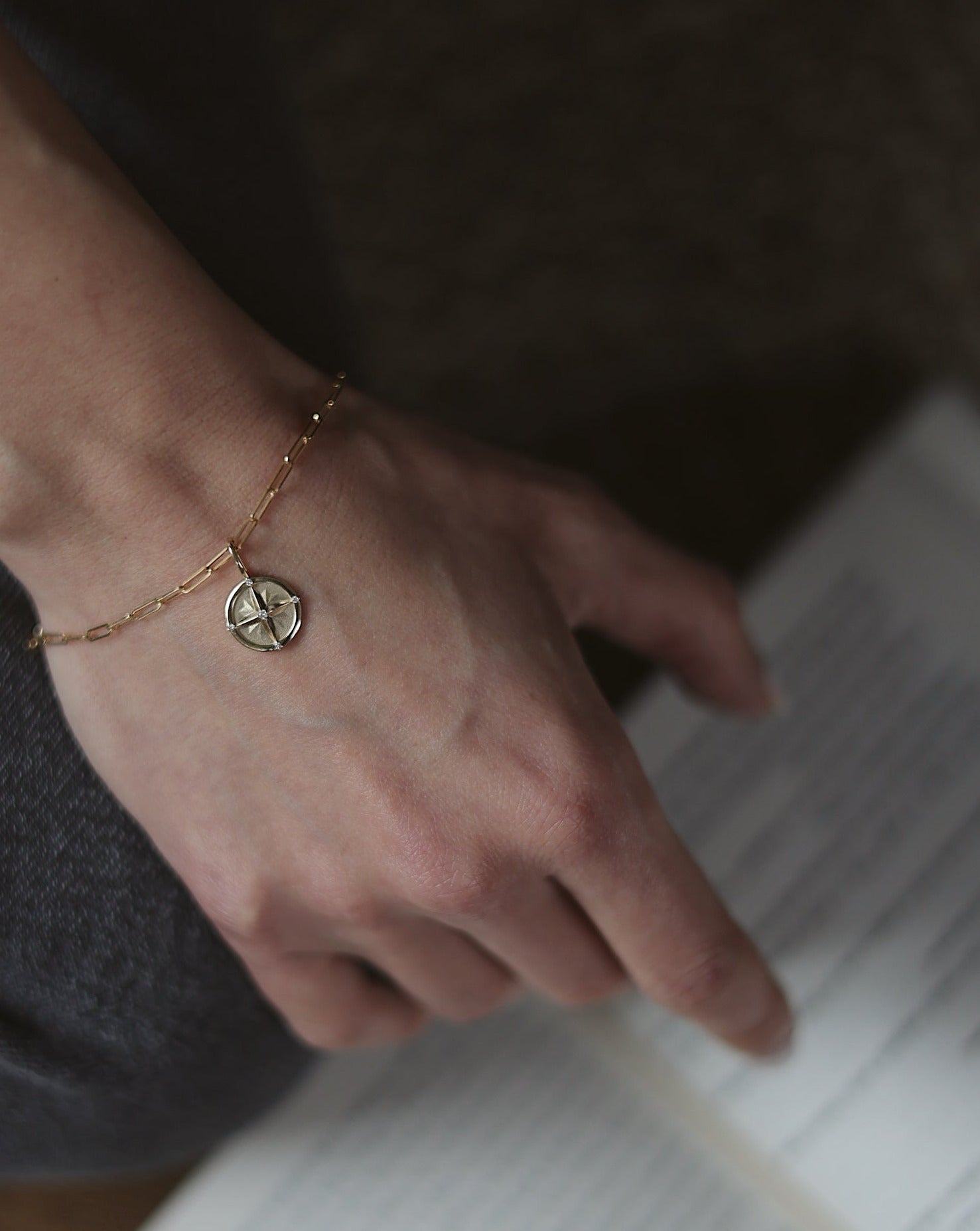 14K gold and diamond compass charm on a paperclip chain bracelet on a female models hand, fine jewelry by Sincerely Chain Co.