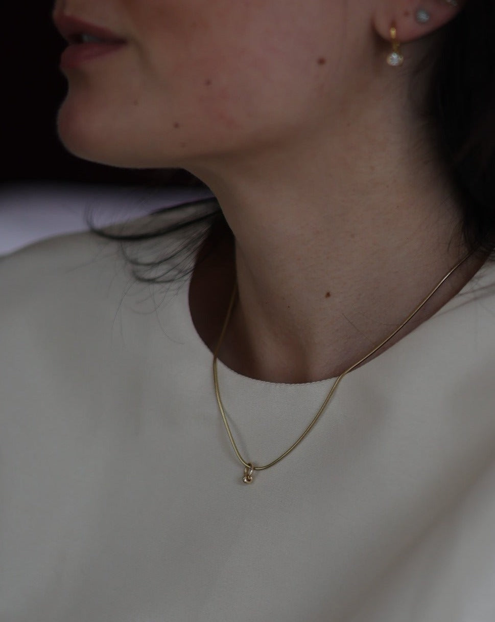 A dainty 14k gold snake chain featuring a roundel charm worn on a female model, elegant layering jewelry by Sincerely Chain Co.