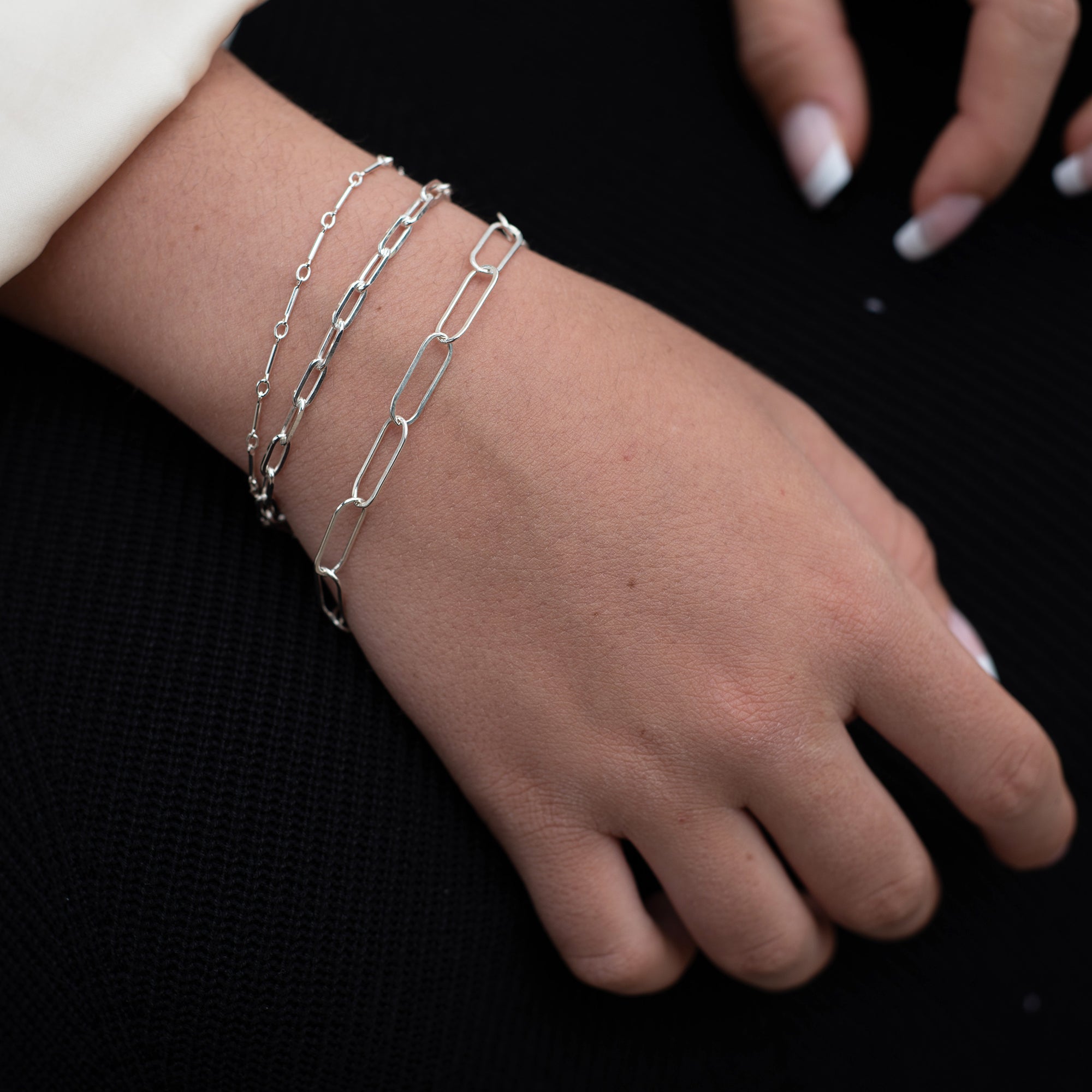 women wearing three sterling silver bracelets with paperclip style links and french manicure