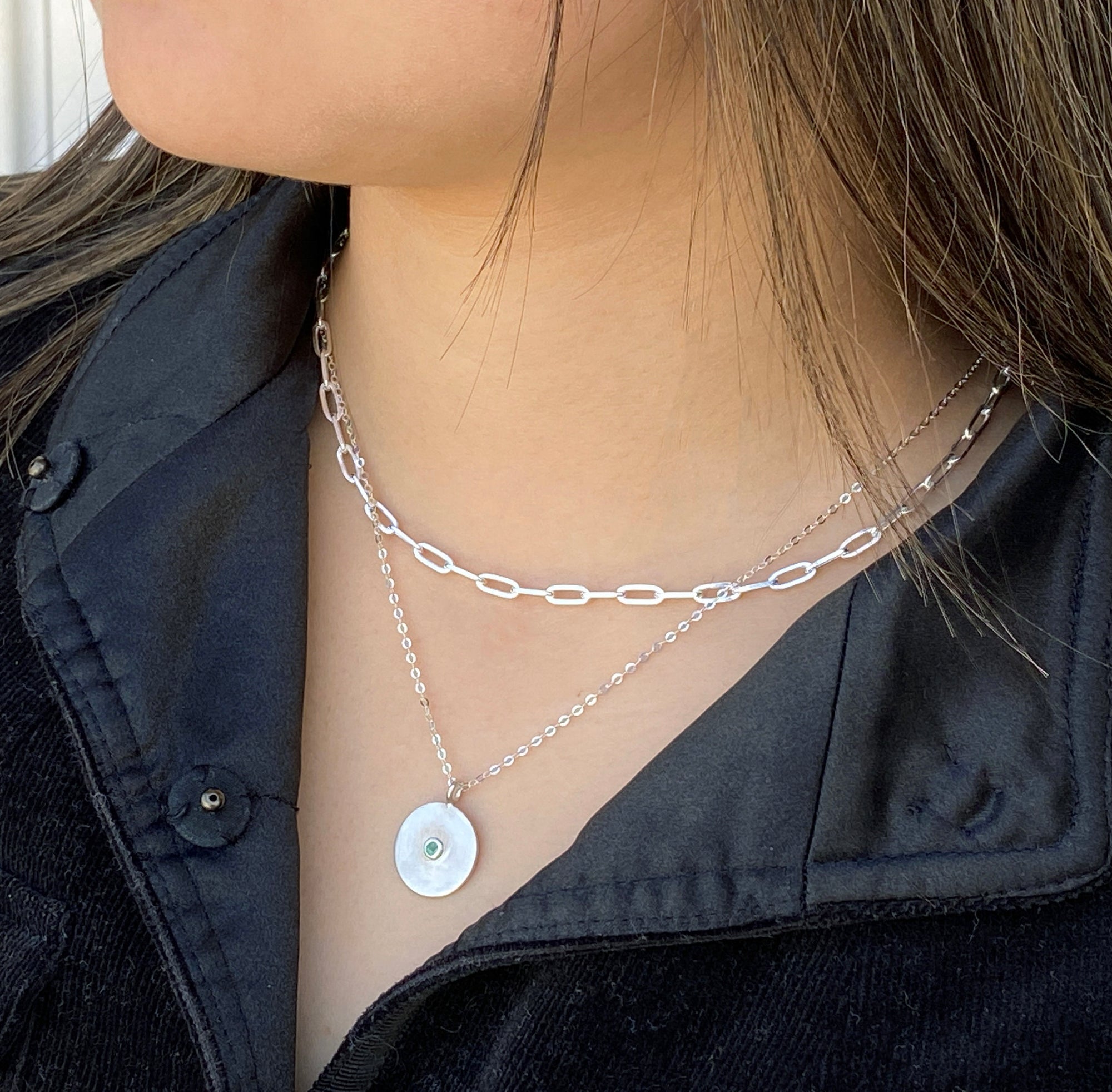 women wearing two silver necklaces featuring a disc pendant set with a tiny emerald