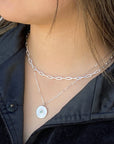 women wearing two silver necklaces featuring a disc pendant set with a tiny emerald